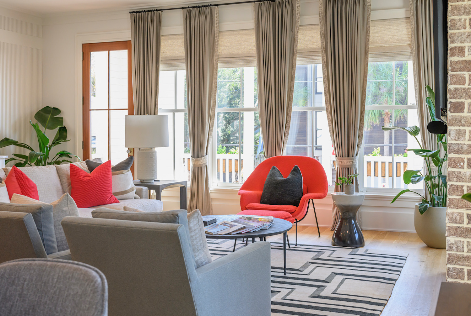 Living room with large windows, beige curtains, colorful chairs, and a patterned rug.