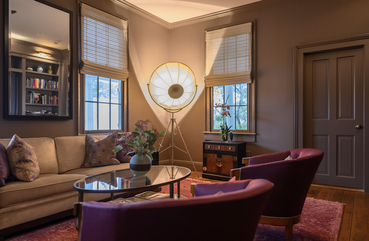 Living room with beige sofa, two pink armchairs, a round coffee table, and a floor lamp between two windows.