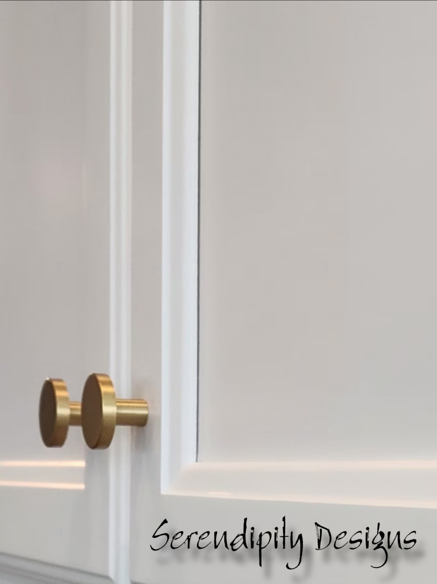 White cabinet door with gold handles, slightly open, with a white wall behind it.