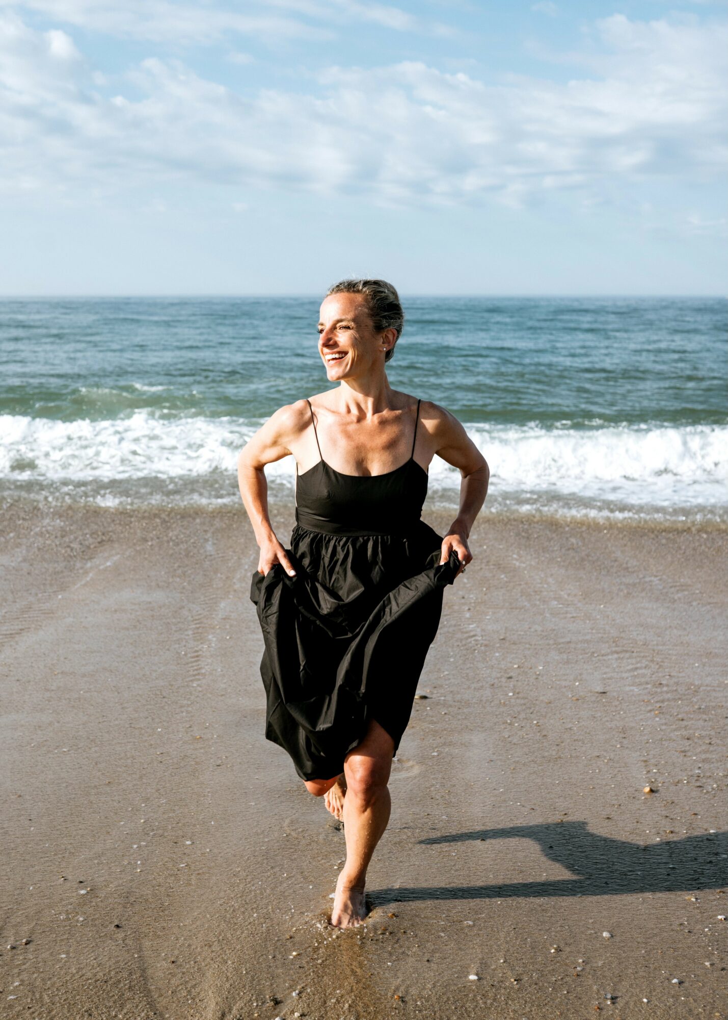 Woman in a black dress walking on the beach with ocean and sky in background