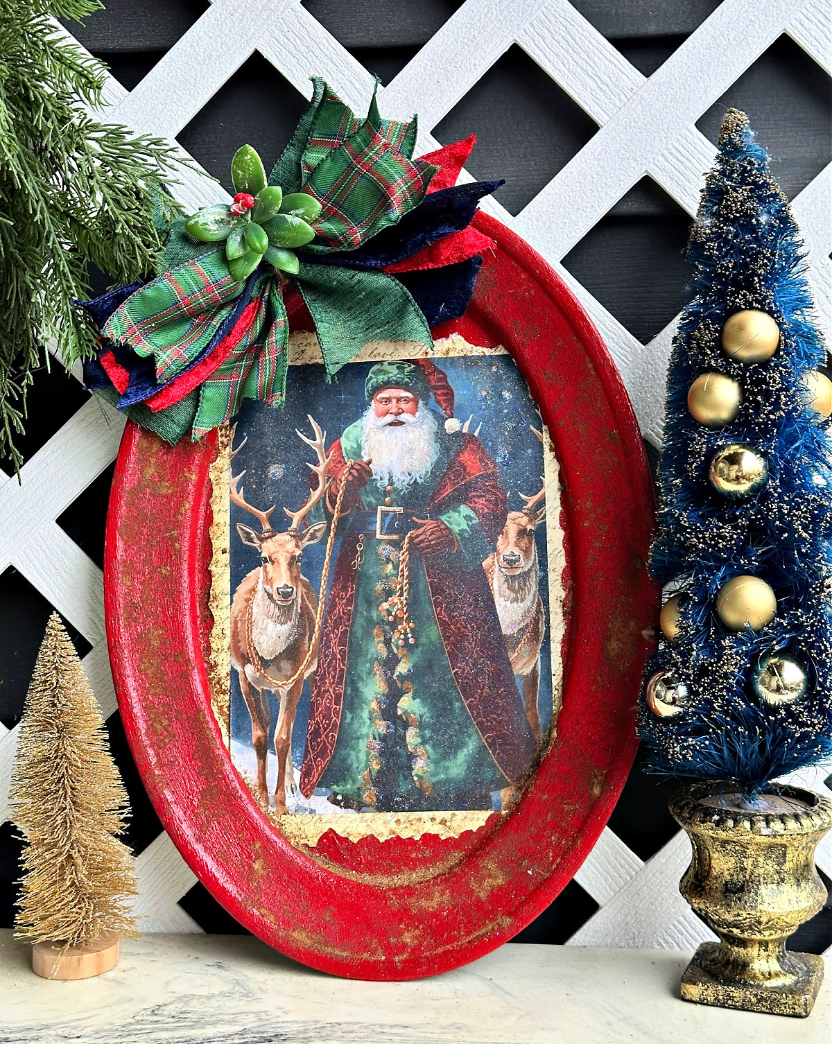 Decorative Christmas frame with Santa Claus and reindeer, adorned with a green plaid bow and festive ornaments, against a white lattice background.