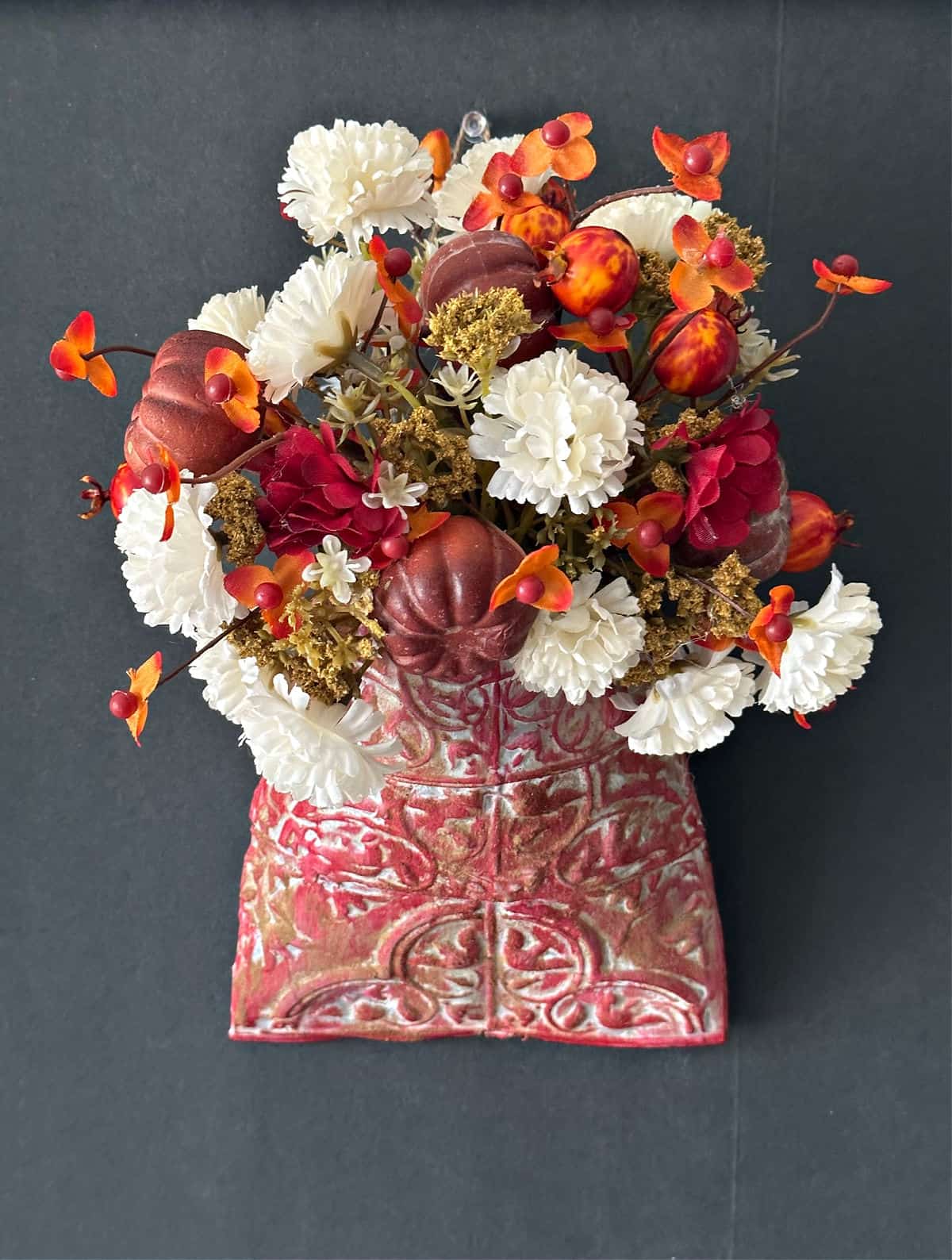 Flower arrangement with red, white, and orange flowers in a decorative pink vase against a dark background.
