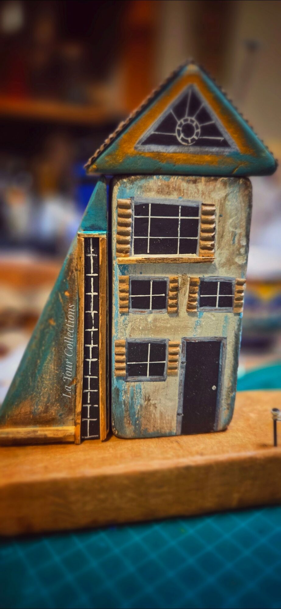 Decorative house-shaped object with geometric patterns and textured surfaces, placed on a wooden surface.