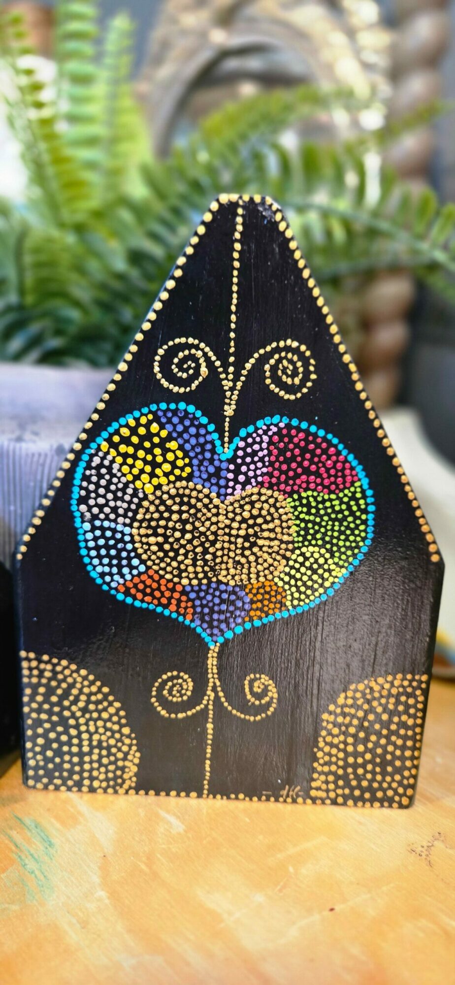 Decorative object with a colorful, dotted design of a bird on a black background, surrounded by gold accents.