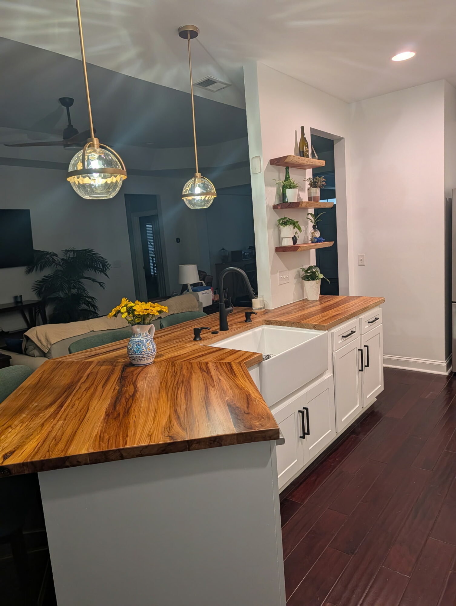 Kitchen with white cabinets, wooden countertop, and hanging pendant lights, with a window and open shelving on the wall.