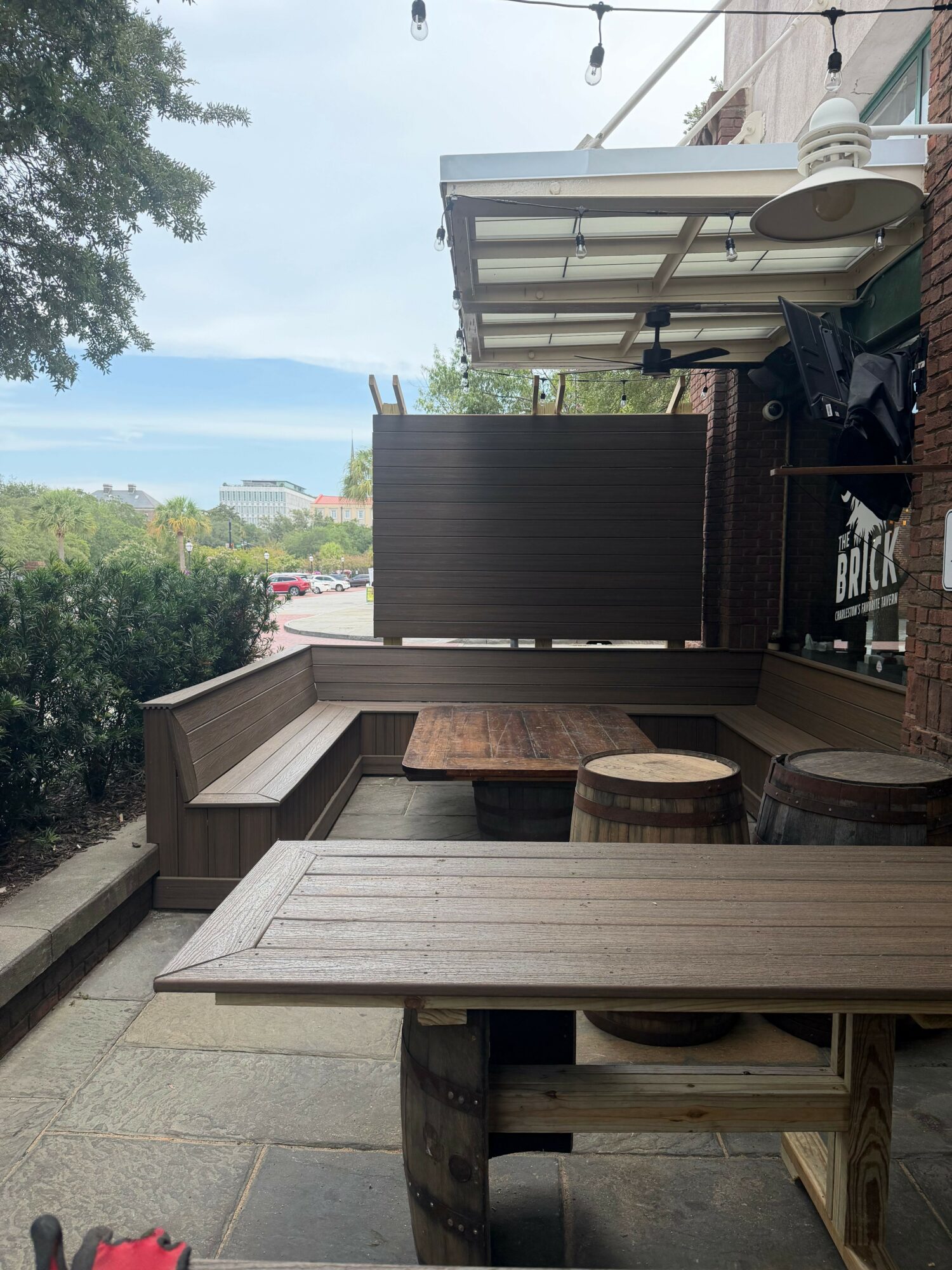 Outdoor seating area with wooden tables and benches, umbrella, and view of trees and sky in the background.