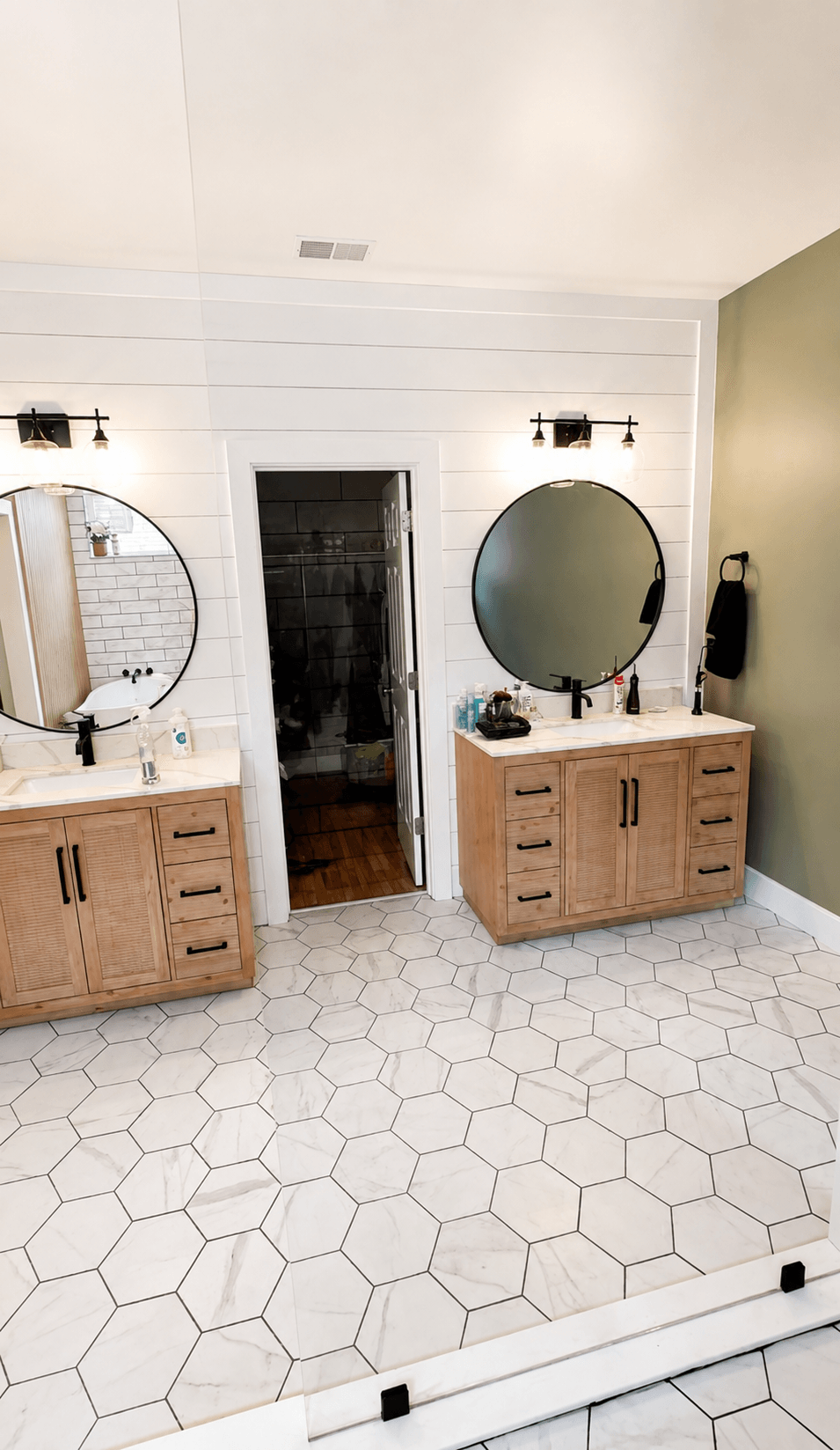 Bathroom with two wooden vanities, round mirrors, hexagonal tile floor, and a door in the center.
