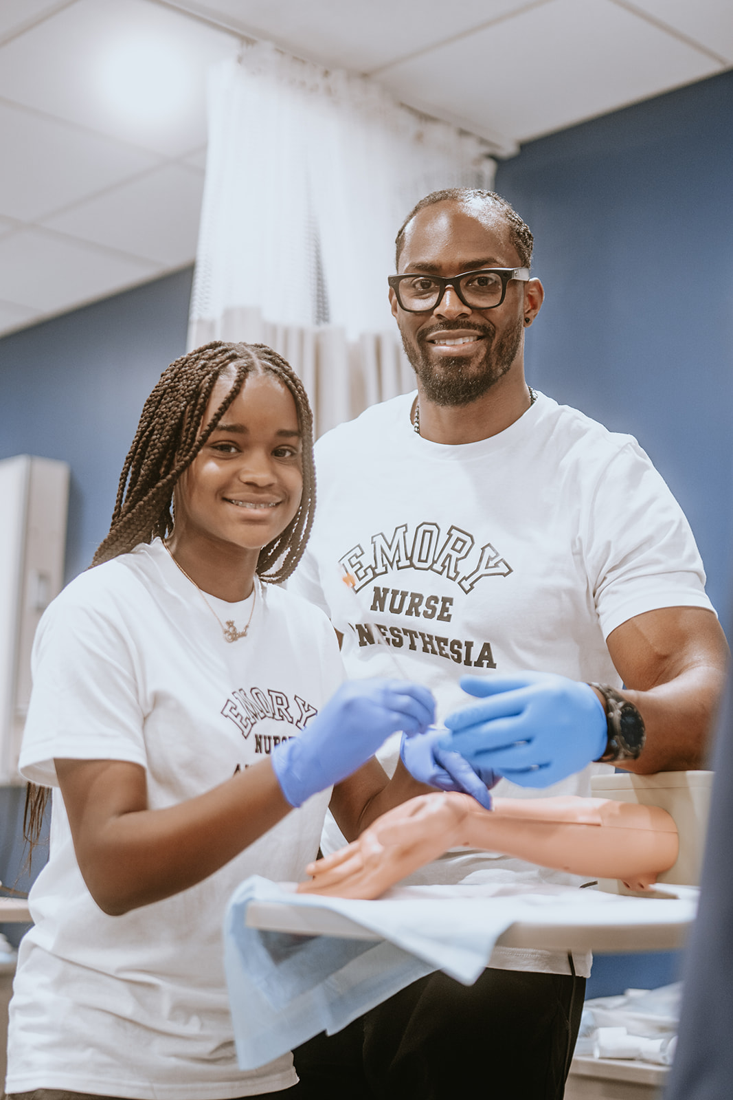 Two people, a young girl and an adult man, smiling and wearing white shirts, in a medical setting.