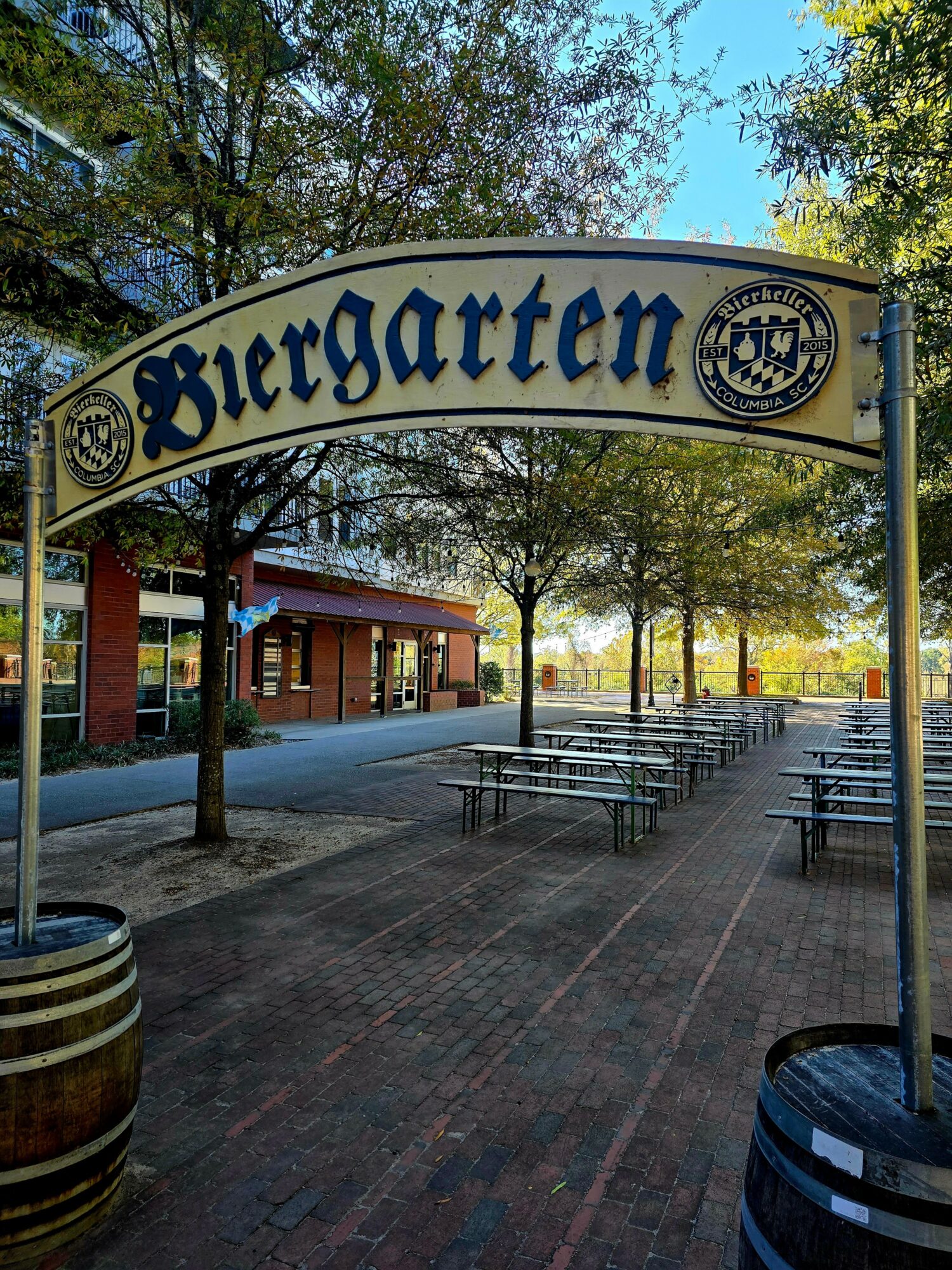 Outdoor seating area with tables and benches under trees, sign reads