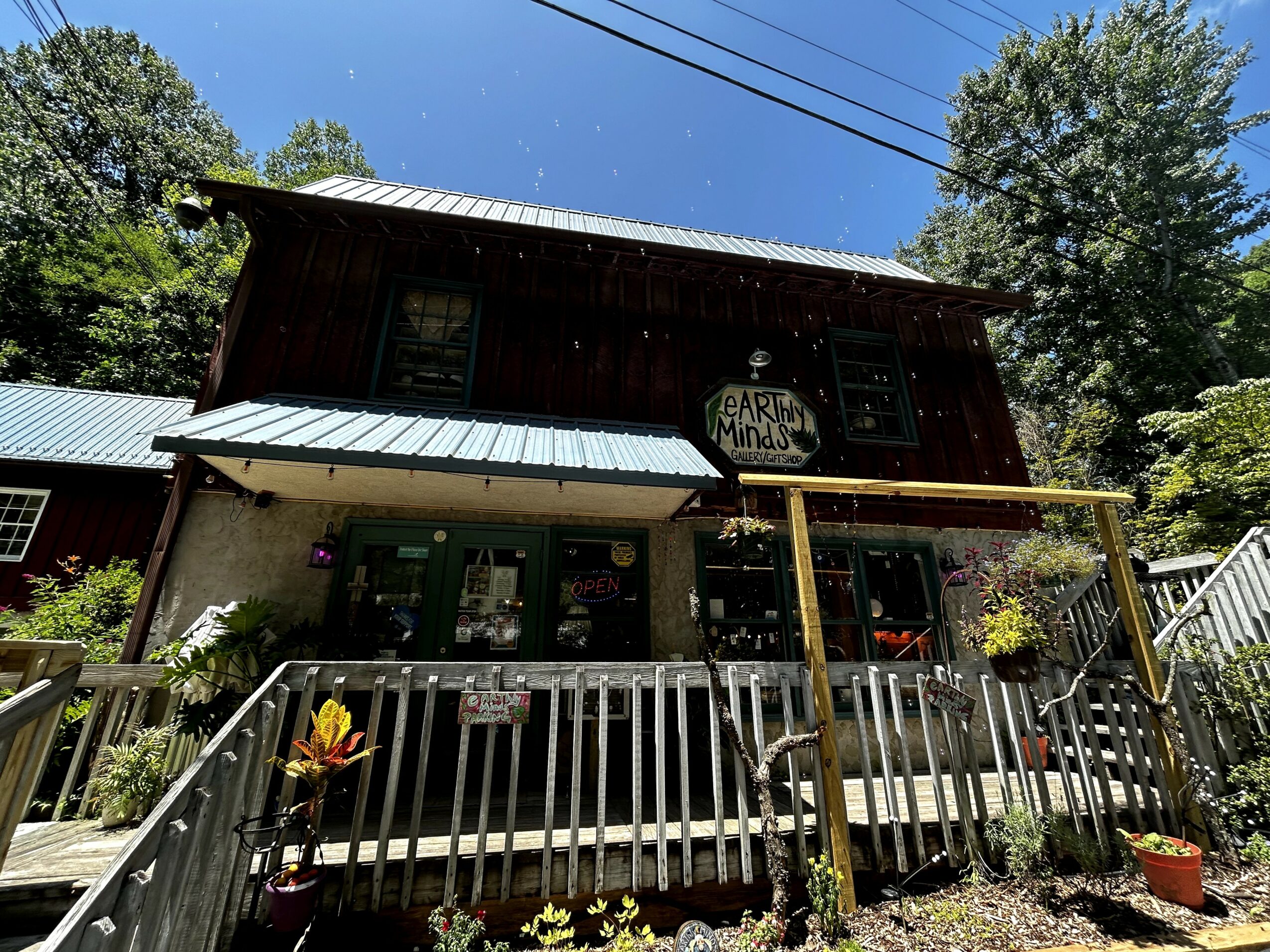 Two-story building with a sign reading 'Artisan Market,' surrounded by trees and a wooden deck with potted plants.