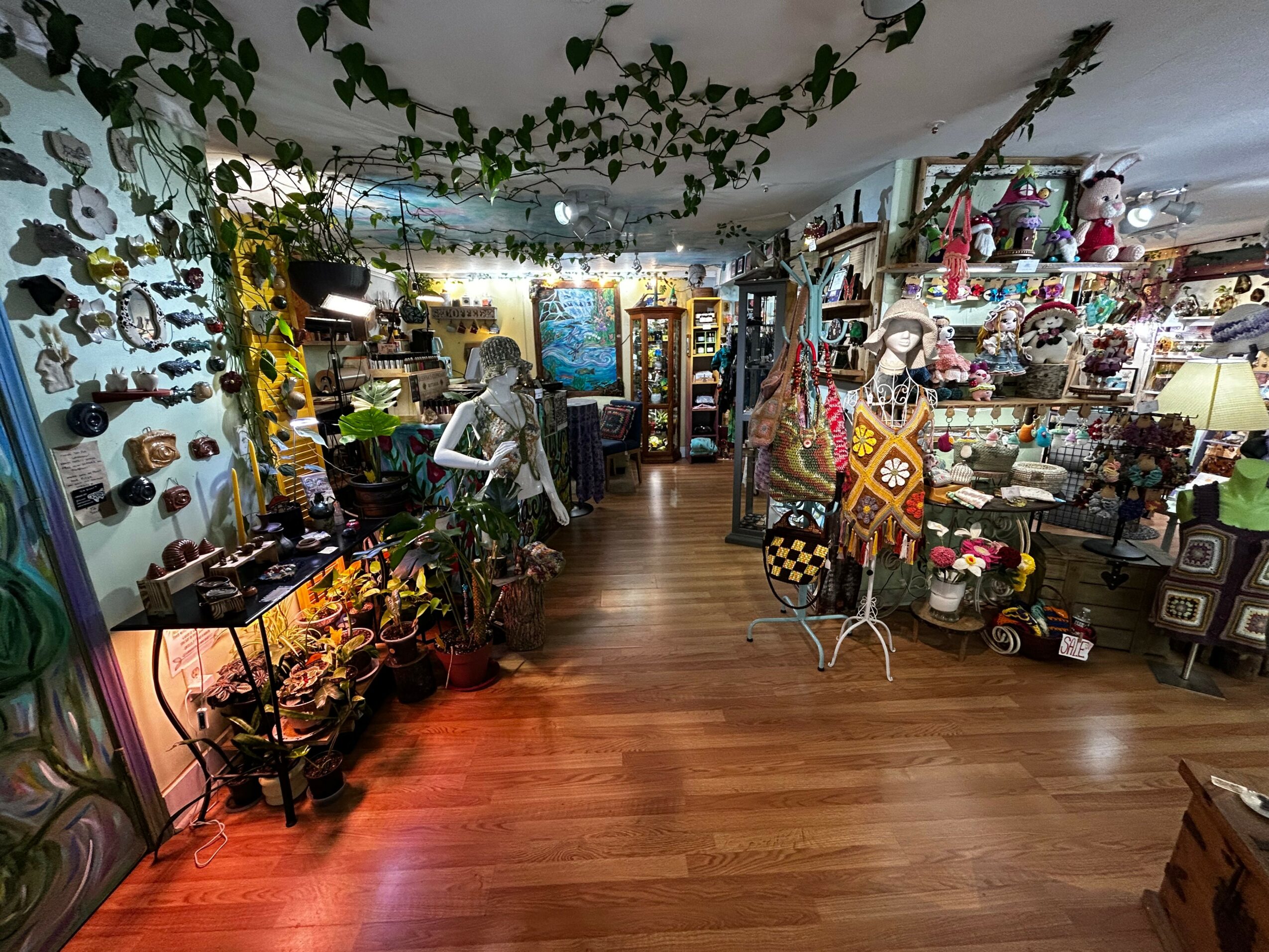 Interior of a store with shelves and displays of decorative items, plants, and textiles, with wooden flooring and ceiling decorations.
