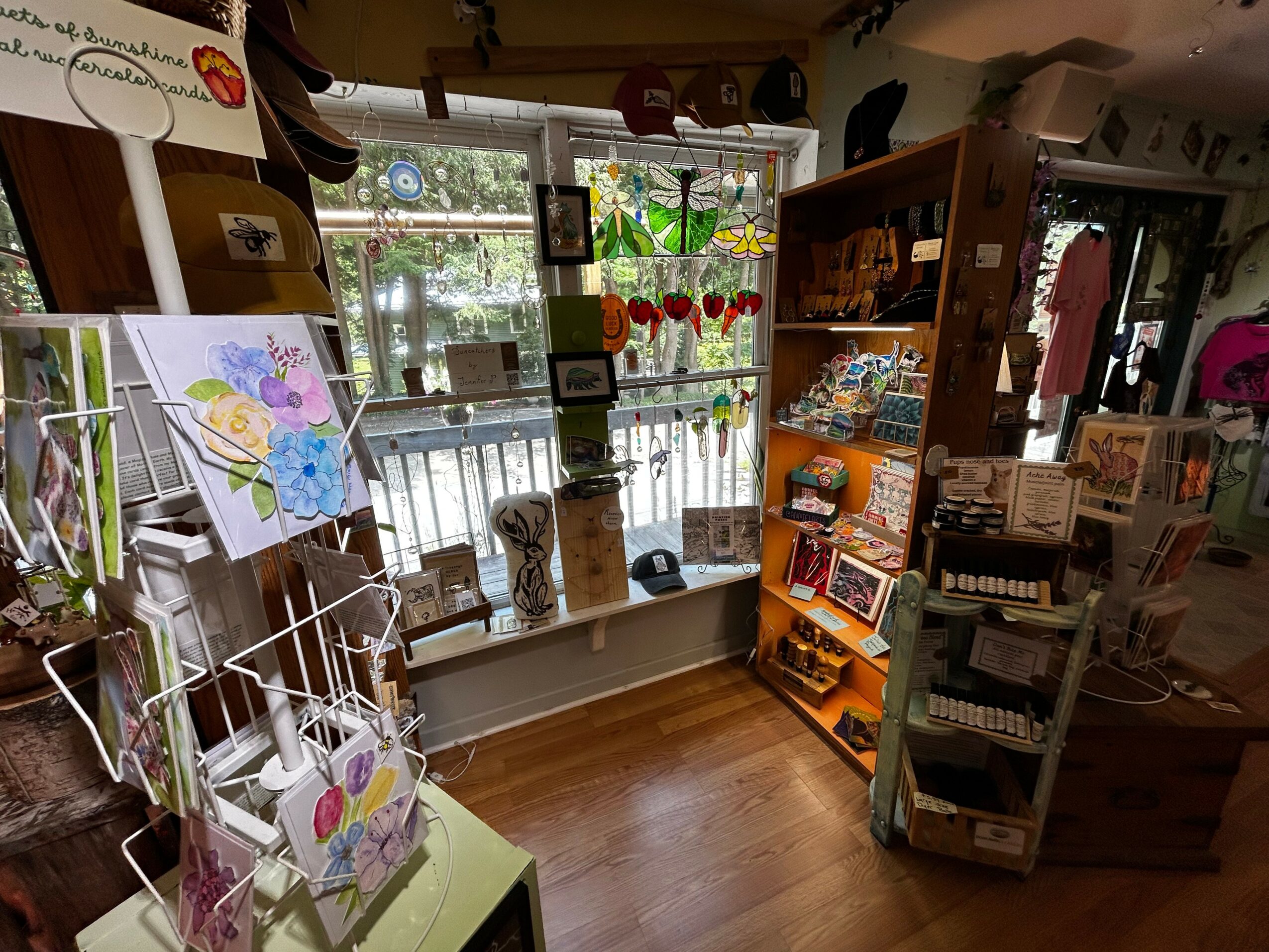 Interior of a store with shelves, artwork, and a window with decorations, wooden floor, and various items displayed.