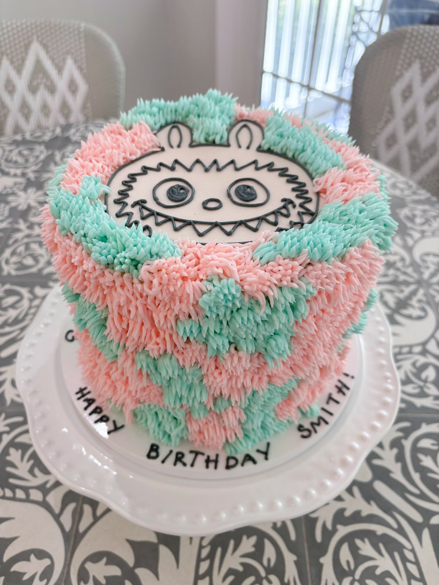 Colorful birthday cake with a bear face design, pink, green, and white frosting, on a white plate with birthday message.