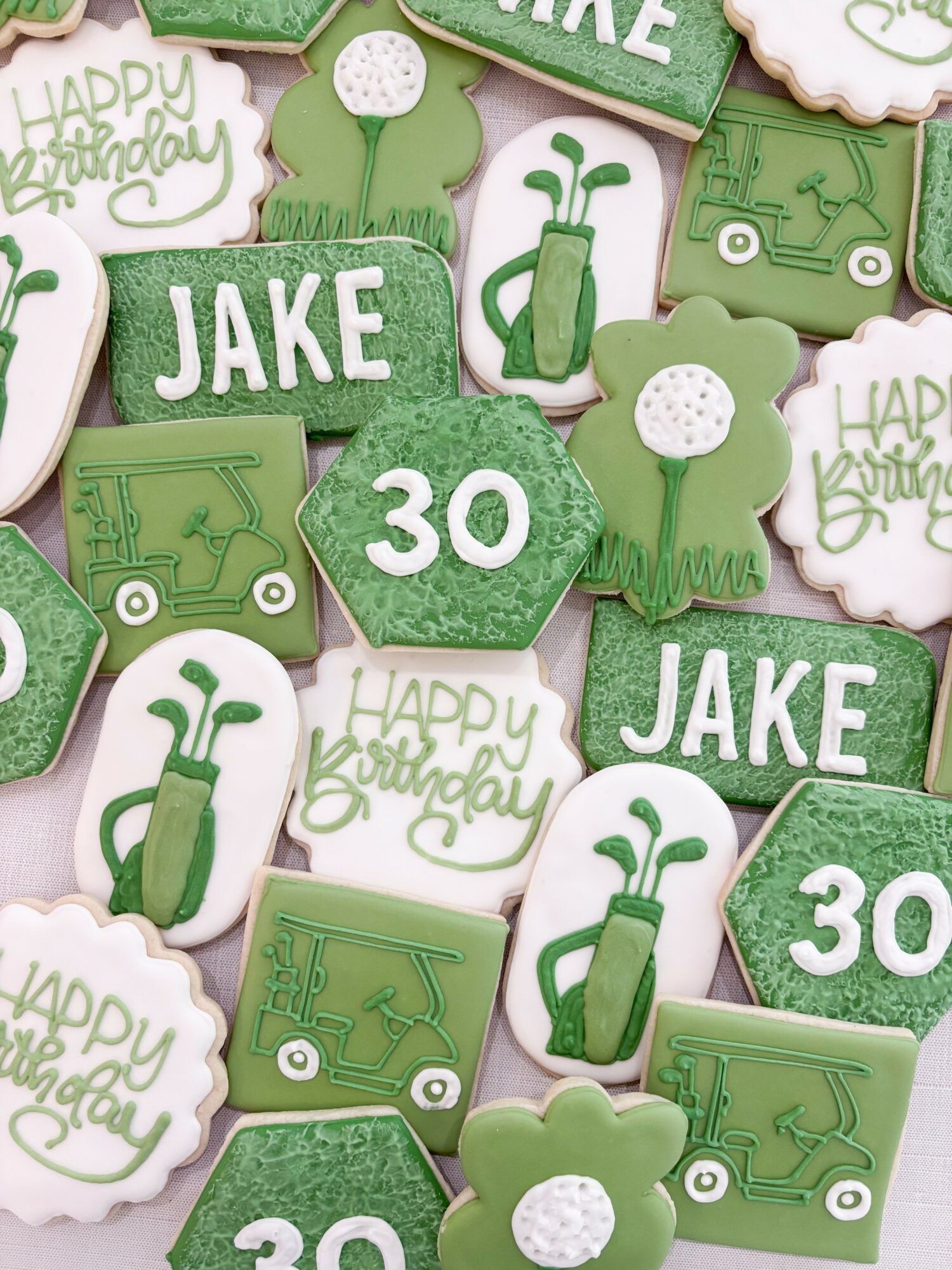 Collection of green and white cookies with golf-themed and birthday messages, including the name Jake and age 30, decorated with golf and grass designs.