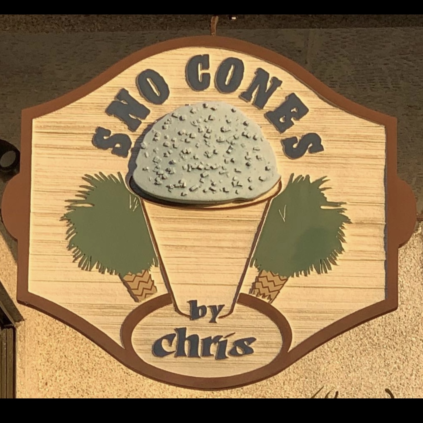 Wooden sign with a cone-shaped ice cream topped with sprinkles, two trees, and text reading