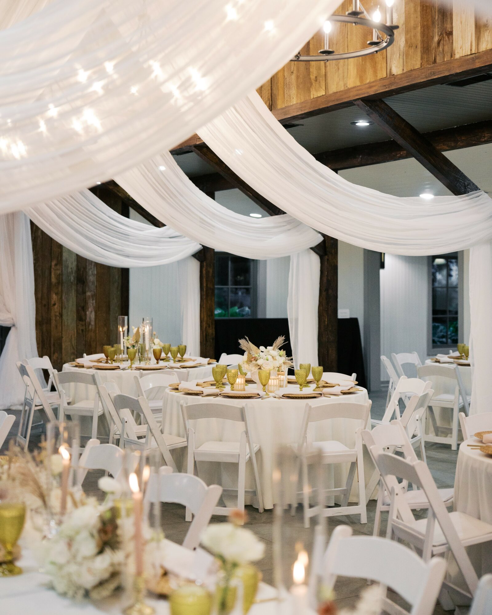 Elegant event space with white draped fabric ceiling, round tables with white chairs, and floral centerpieces.
