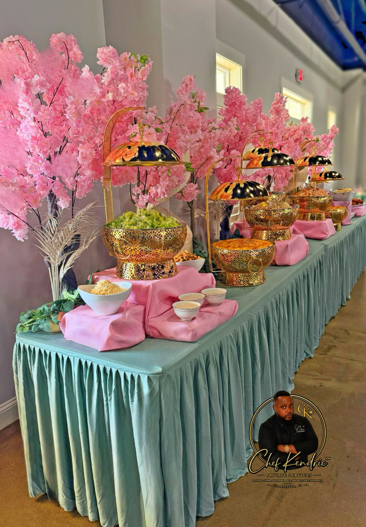 Decorative table with pink artificial trees, glass jars filled with colorful candies, pink napkins, and small bowls, set against a light-colored wall.