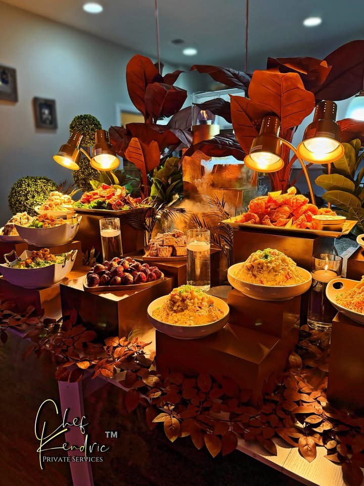 Display of various desserts and food items on a table with decorative plants and warm lighting.