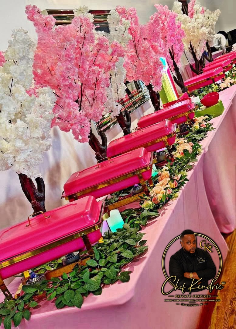 Table decorated with pink and white cherry blossom trees, pink boxes, and floral arrangements, with a pink tablecloth.
