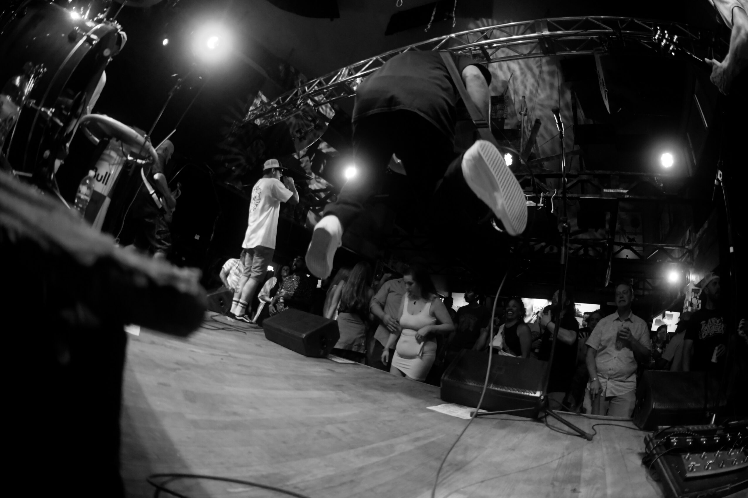 People on stage with lighting and equipment, some standing and others sitting, in a concert or event setting.