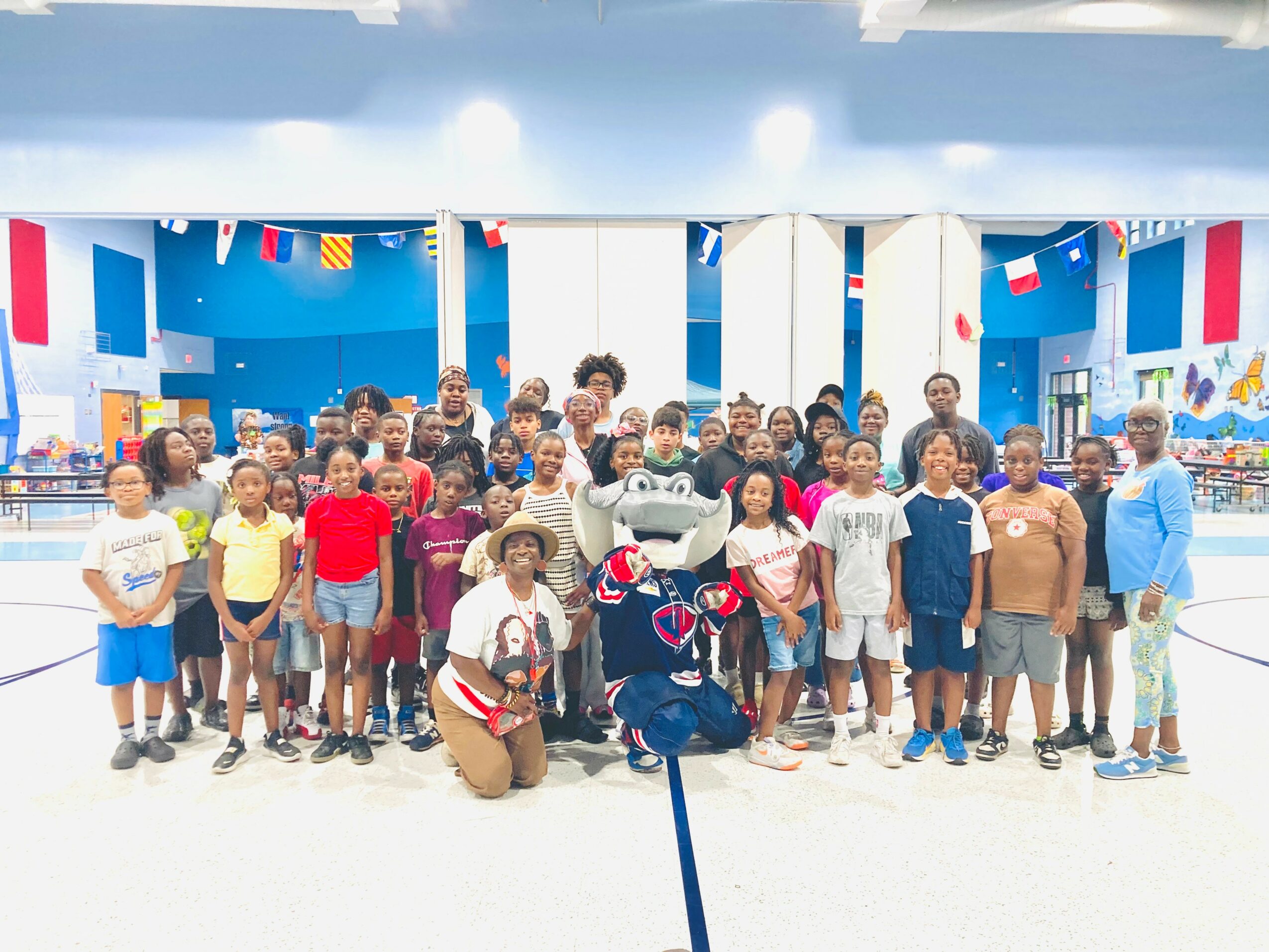 Group of children and adults in a decorated indoor space with flags and banners, some people in costumes, smiling for a photo.
