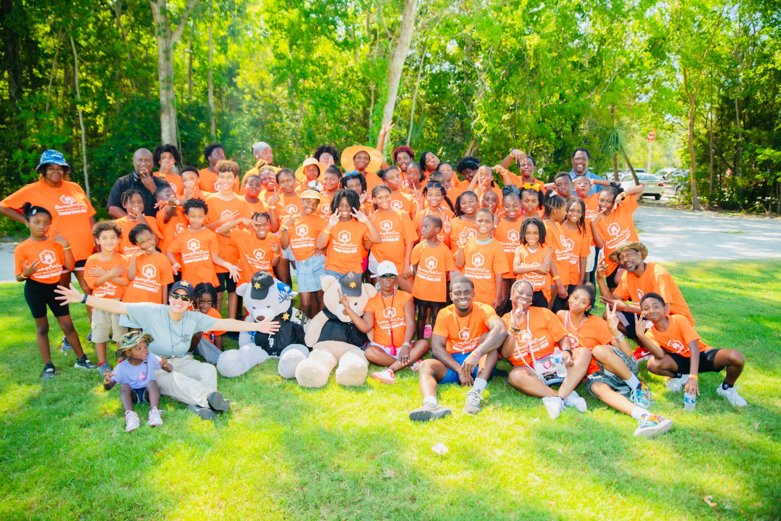 Group of people outdoors in a park, wearing matching orange shirts, with trees and grass in the background.