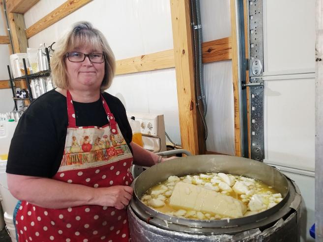 Woman wearing glasses and an apron, cooking in a large pan with butter and potatoes, in a workshop setting.