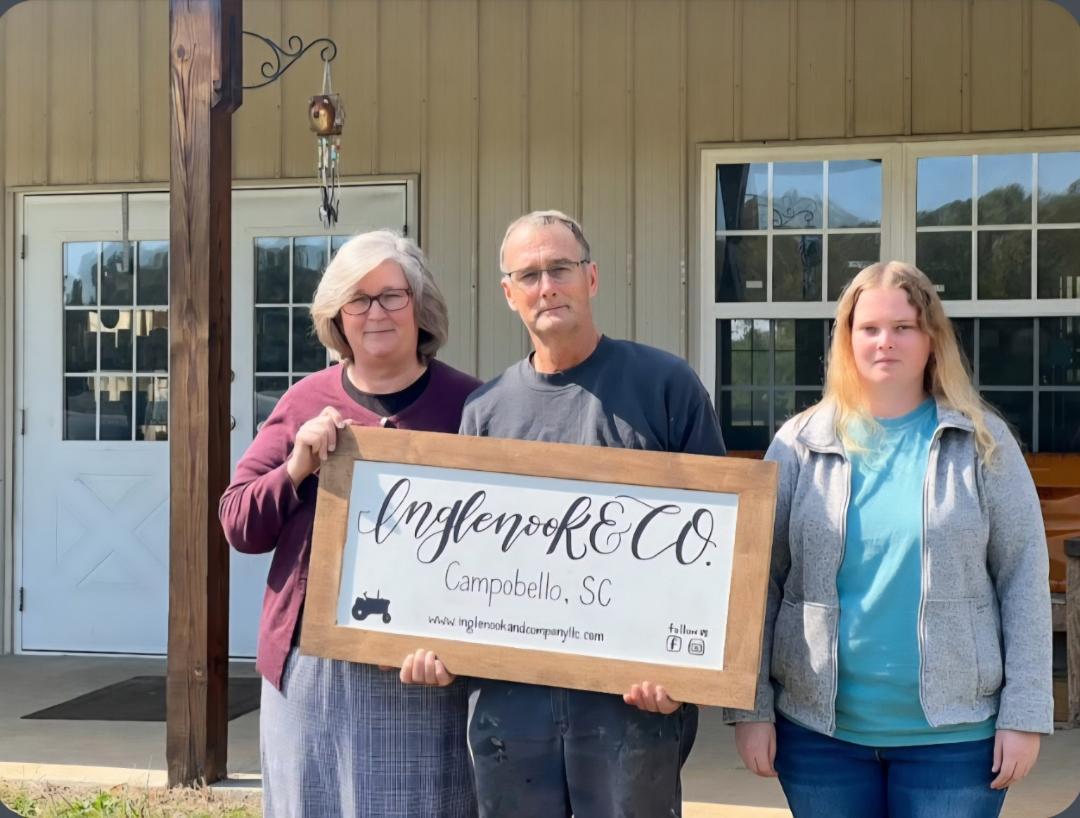 Three people holding a sign outdoors in front of a building with windows and a door.