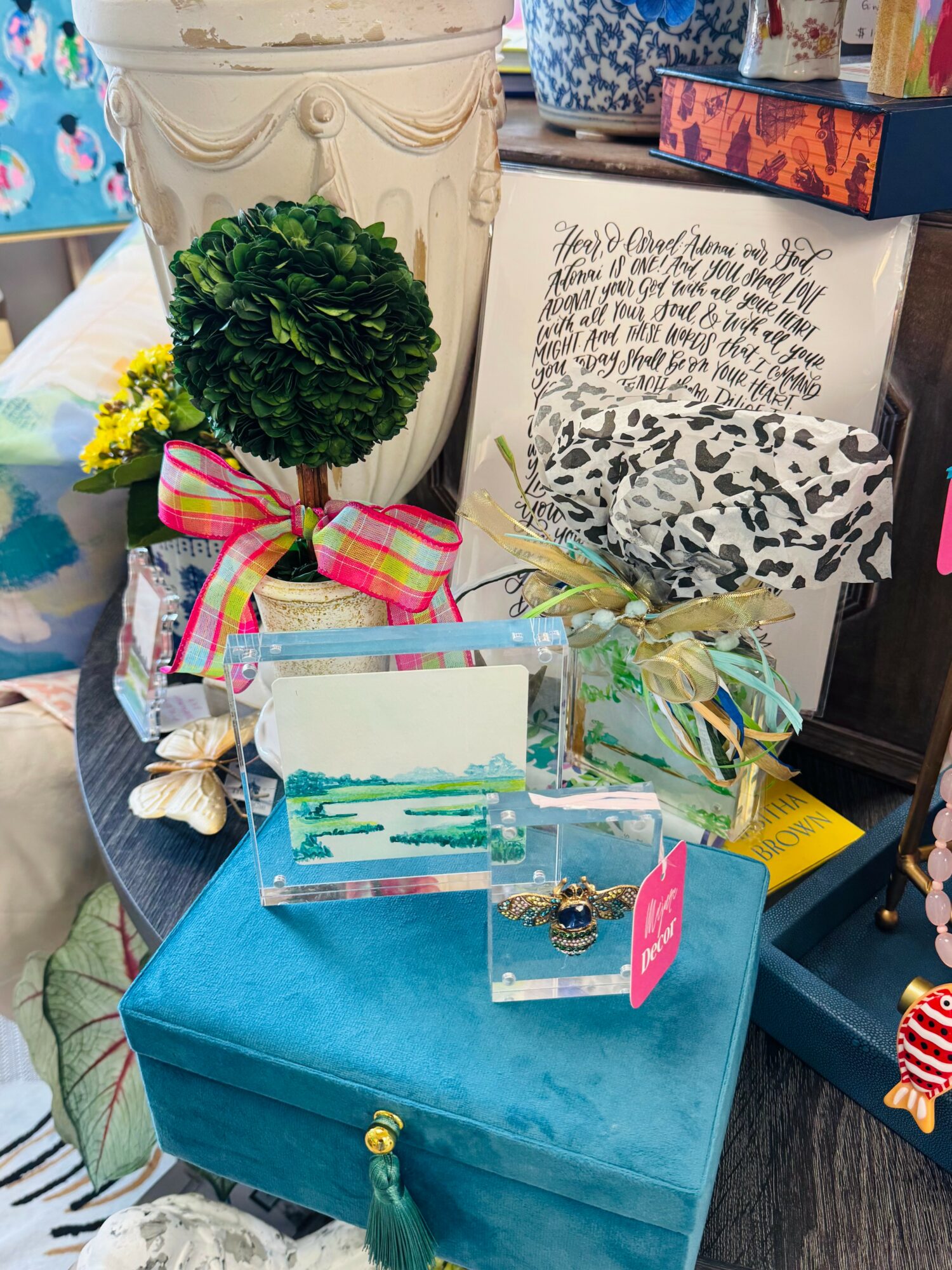 Decorative items including a topiary, framed art, and greeting cards on a blue box, with a plant and other objects in the background.