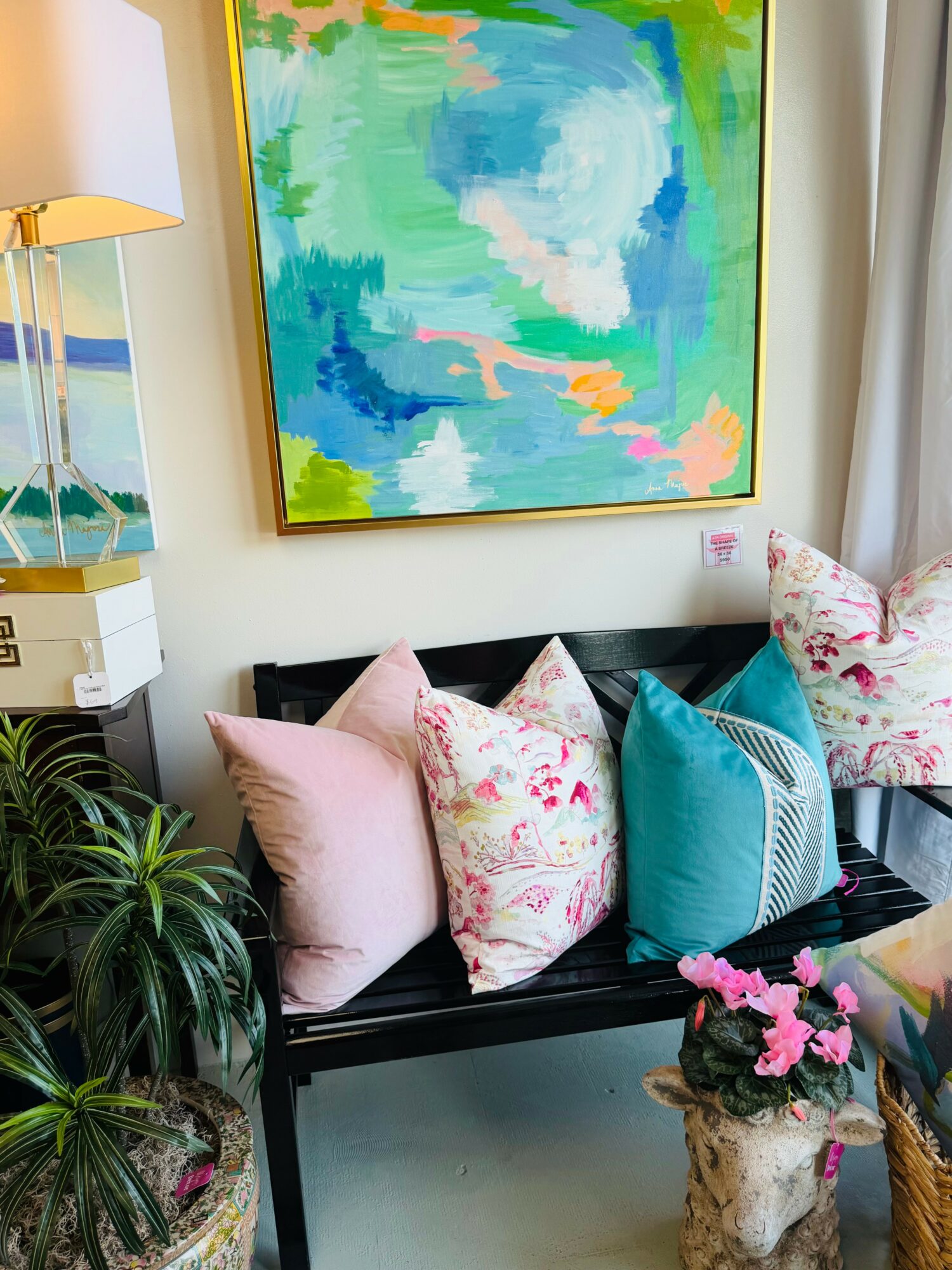 Black bench with pink, blue, and floral pillows, a potted plant, and a flower arrangement in a rustic container.