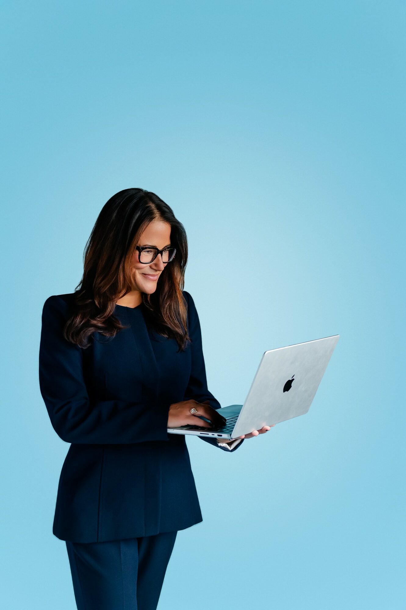 Woman with glasses using a laptop against a blue background.