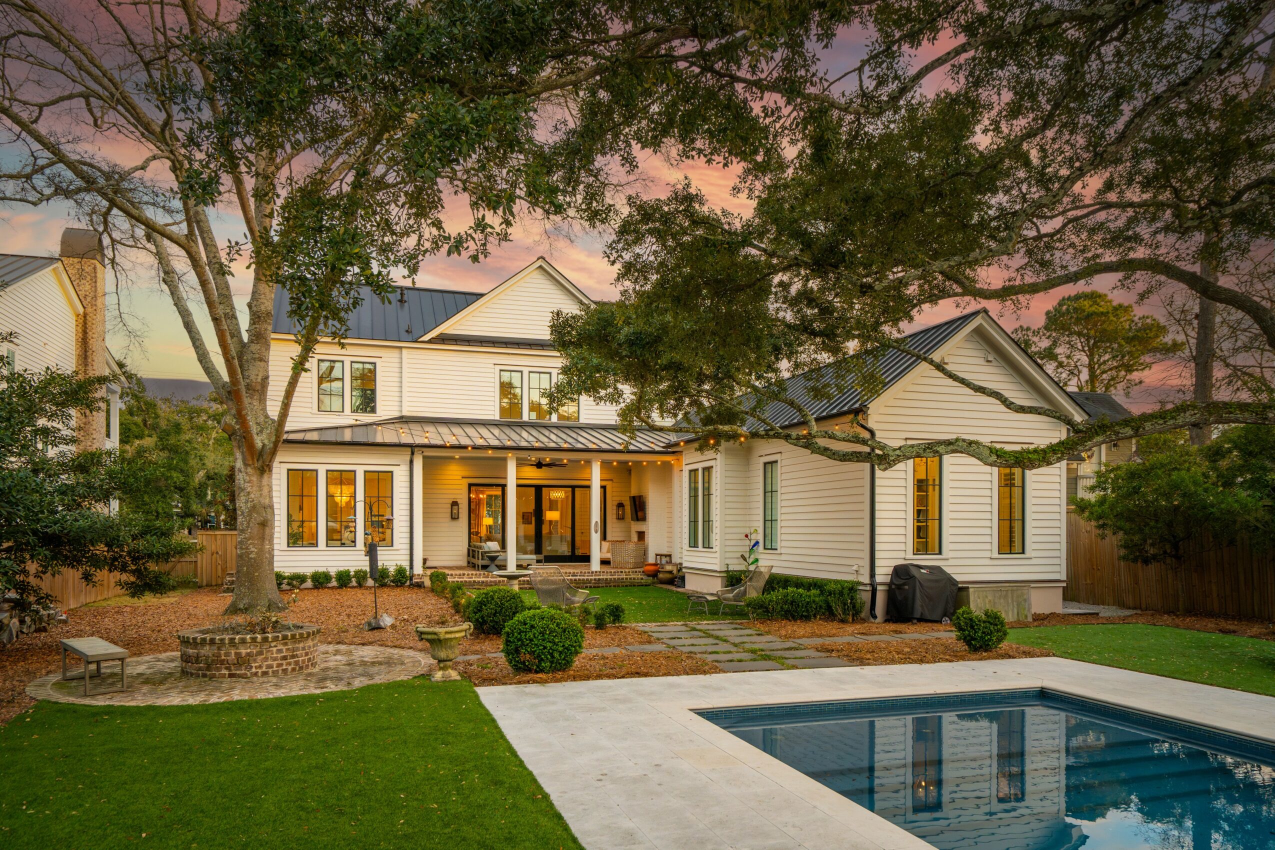 Two-story white house with front porch, surrounded by trees and a lawn, with a swimming pool in the foreground.