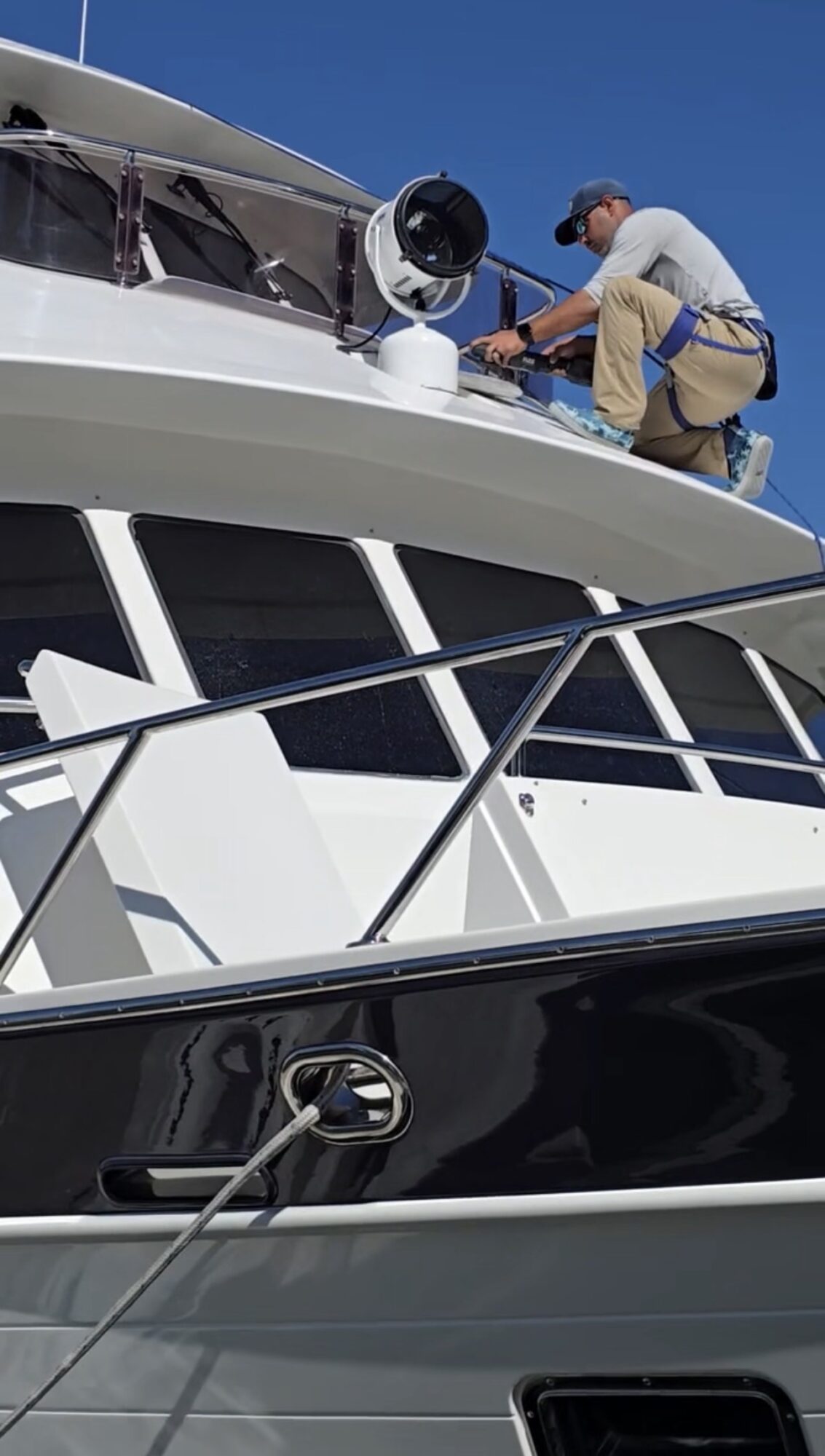 Person working on boat's radar or communication equipment on top deck, clear blue sky background.