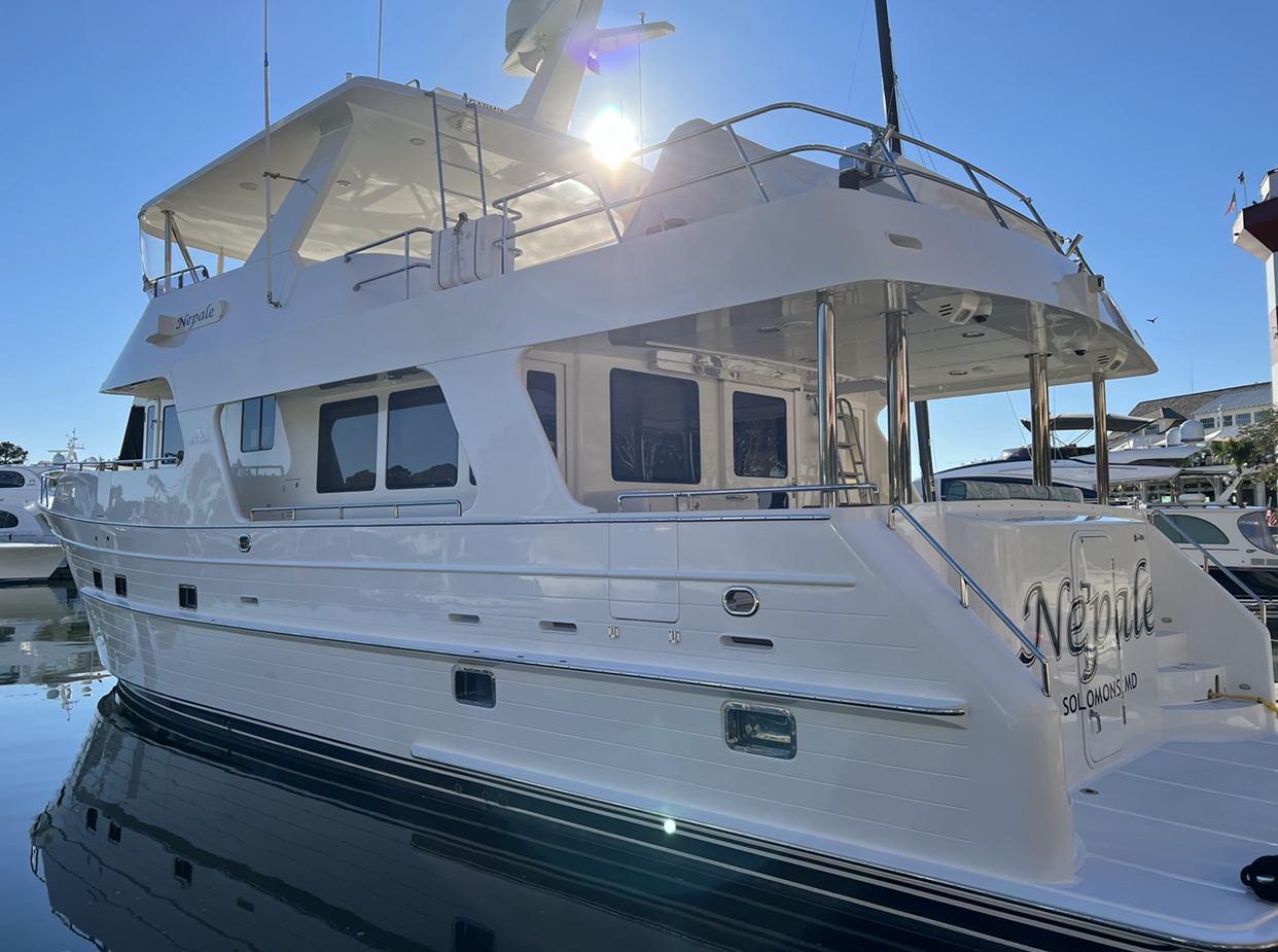 Motor yacht docked at marina with clear blue sky, sunlight reflecting off the water, and other boats nearby.