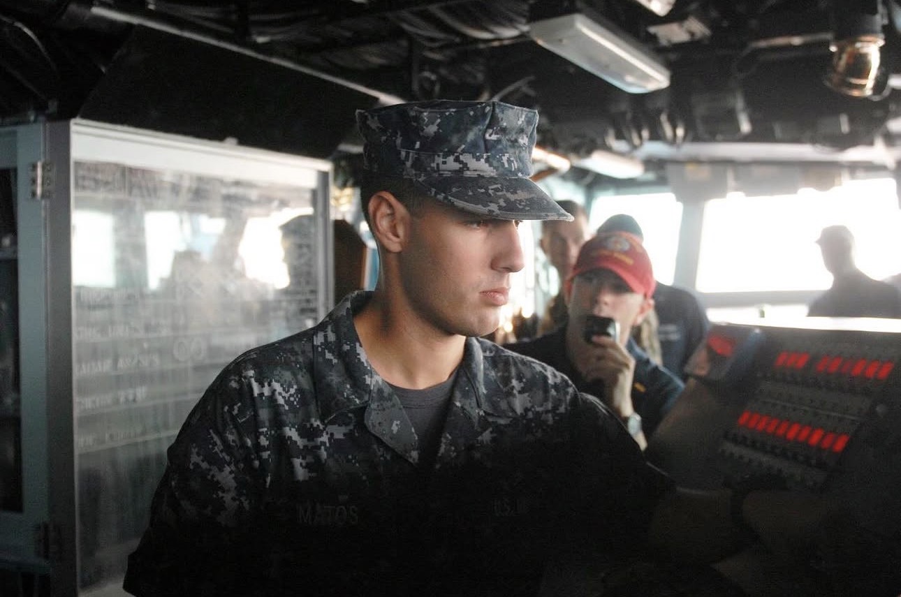 A person in military uniform working with electronic equipment inside a vehicle or control room.
