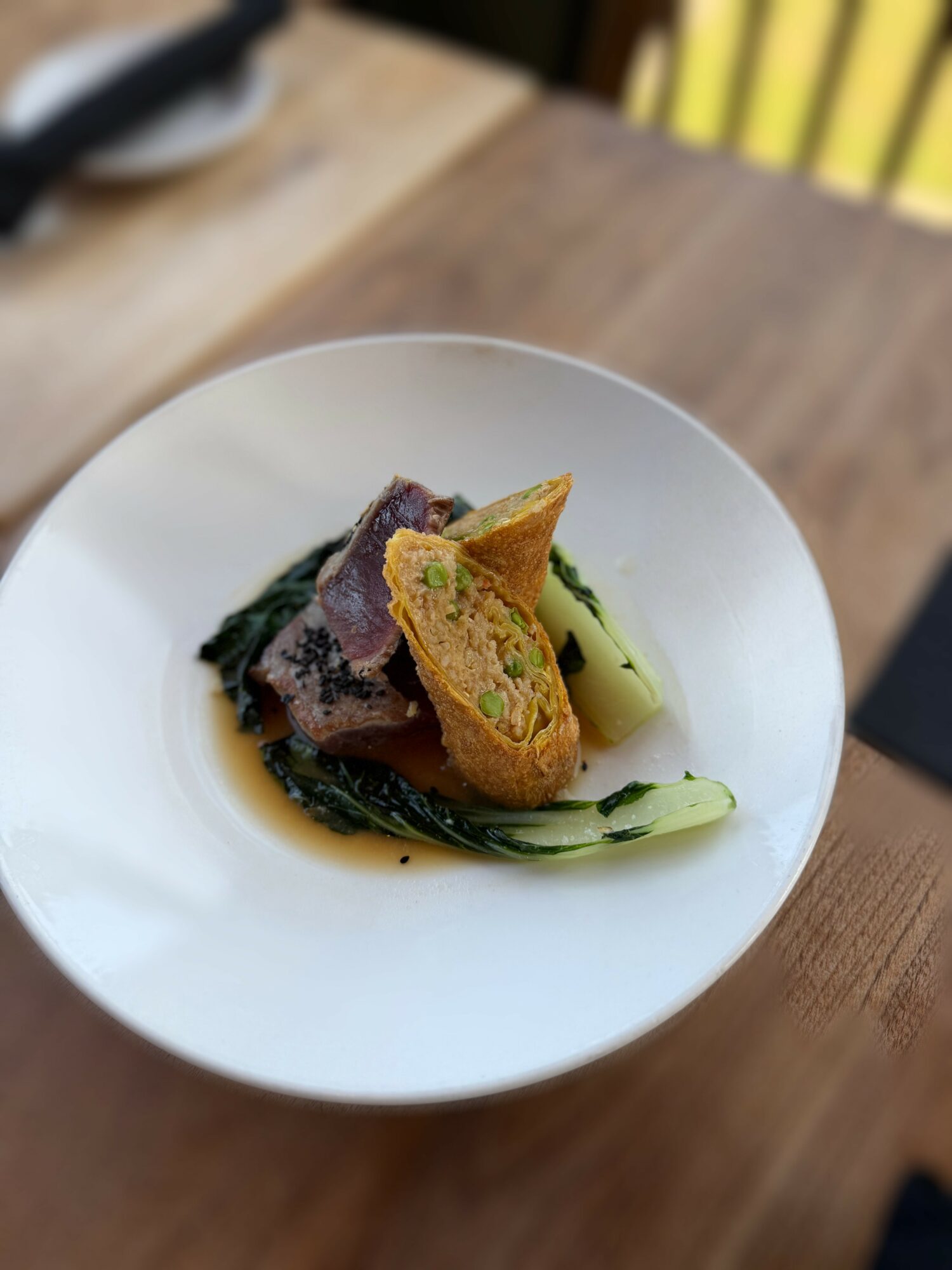 Plate with cooked meat, green vegetables, and two pieces of bread on a white dish, on a wooden table