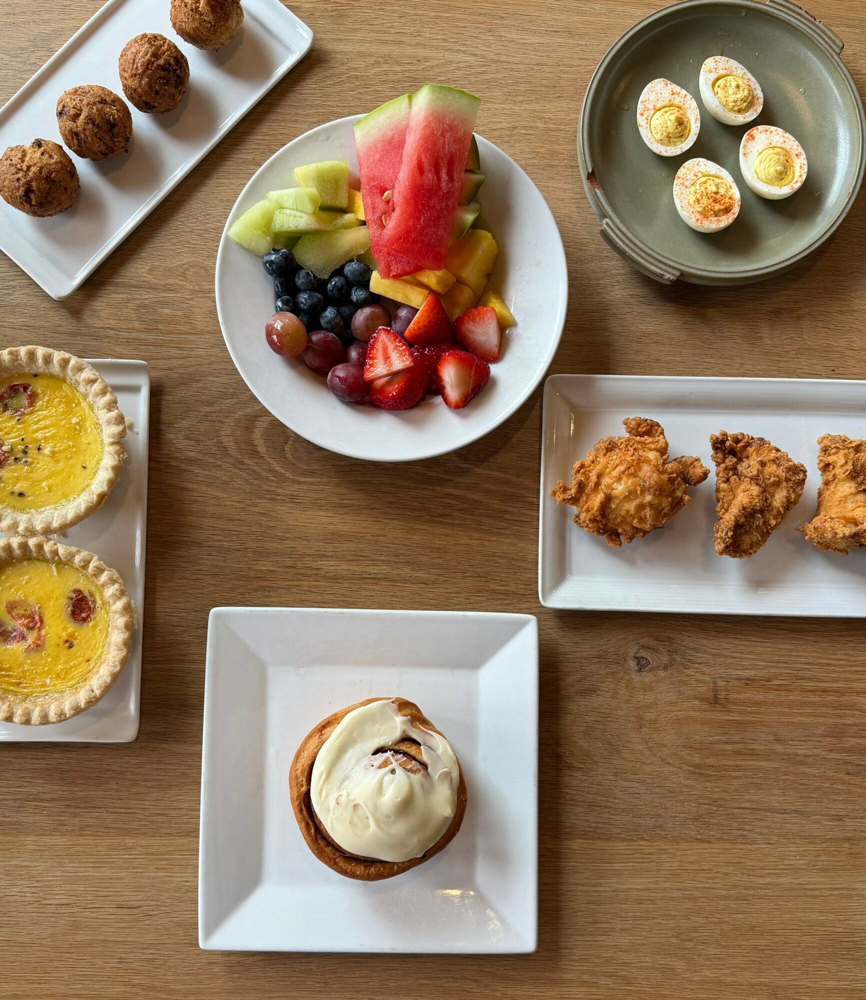 Assorted breakfast foods including fruit, boiled eggs, fried chicken, a cupcake with frosting, and small meatballs on plates.