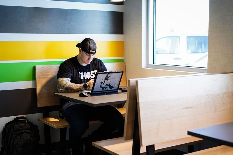 Person wearing headphones working on a laptop in a cafe with colorful striped wall and window view