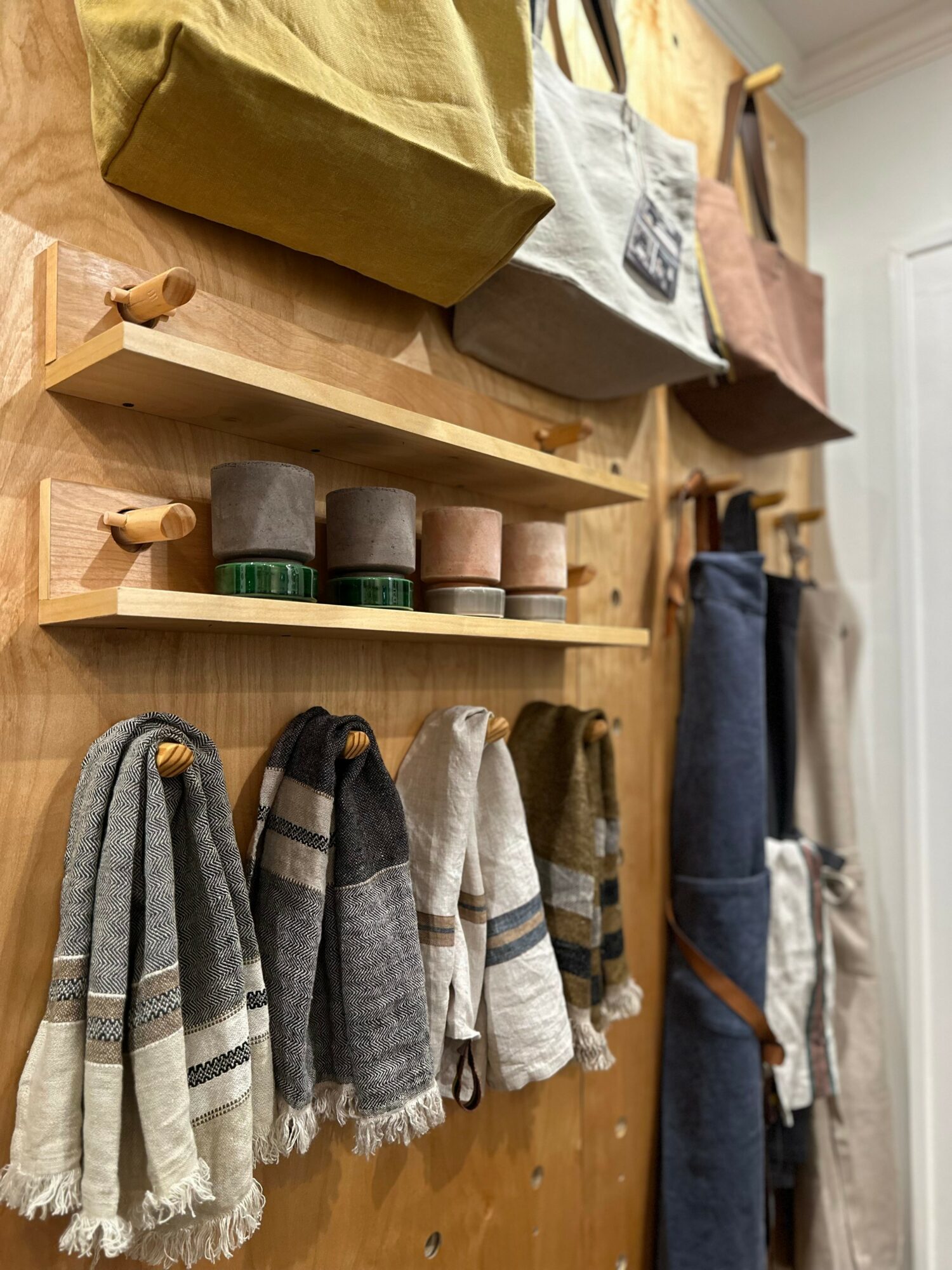Wooden wall with shelves holding bags and scarves hanging below, in a cozy interior setting.