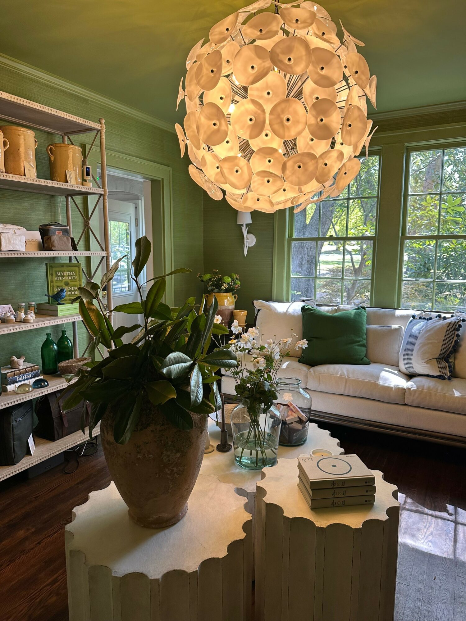 Living room with a large window, green walls, a white sofa, and a flower arrangement on a table.