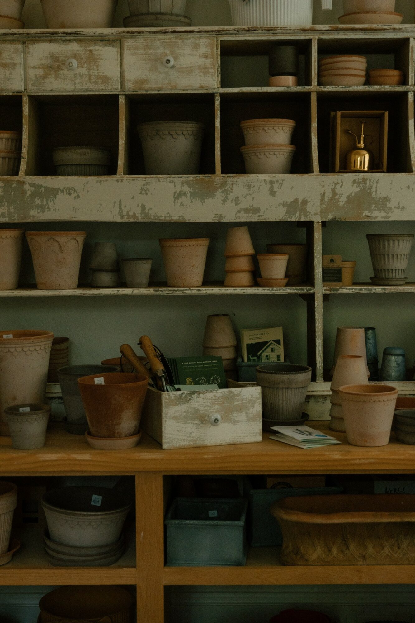 Shelves filled with various pottery pots and containers, some stacked, with a wooden table below holding more pots and tools.