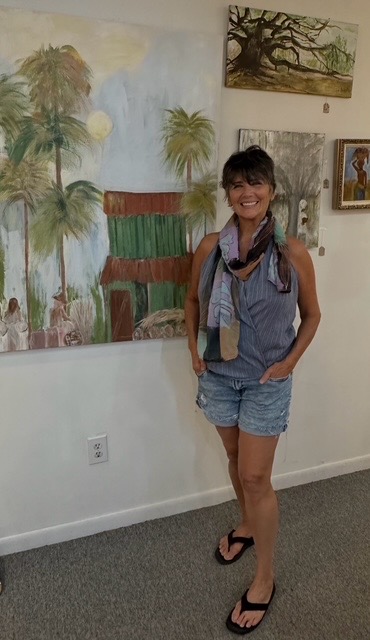 Young woman with short hair, wearing a sleeveless top, shorts, and flip-flops, standing in front of paintings on a white wall.