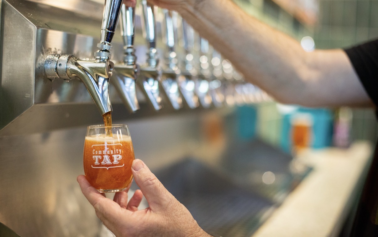 Person filling a glass with beer from a tap, with multiple taps visible in the background.
