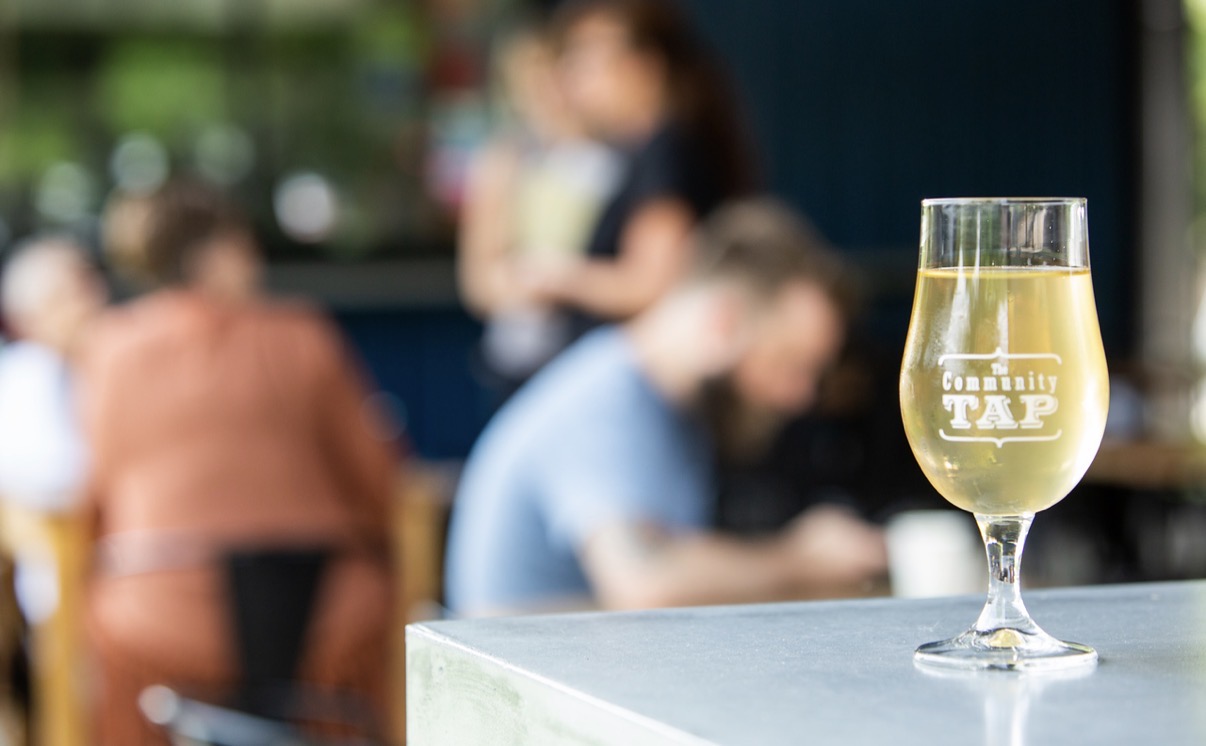 A glass of champagne on a white table with blurred people in the background.
