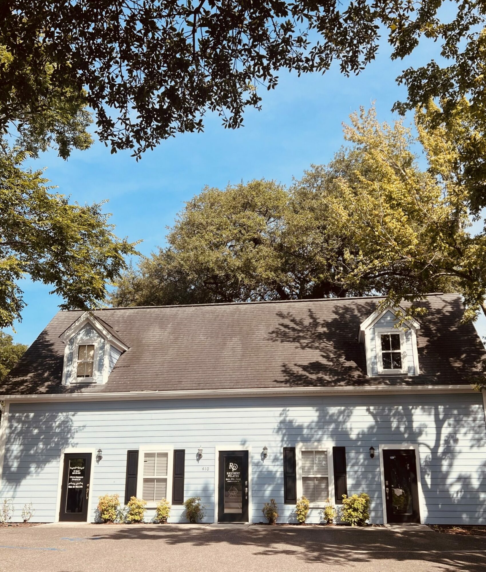 White house with black doors and windows, surrounded by trees with green leaves, under a blue sky.