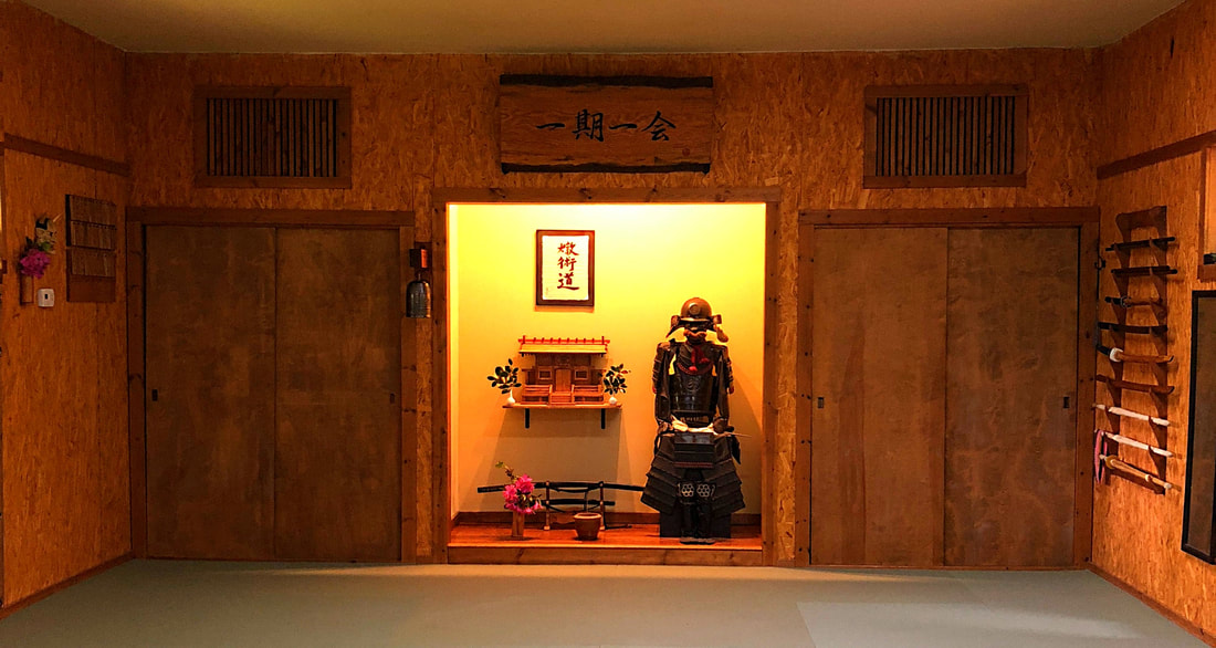 Interior of a traditional Japanese room with sliding doors and a display of armor and decorations, wooden walls, and a hanging scroll.