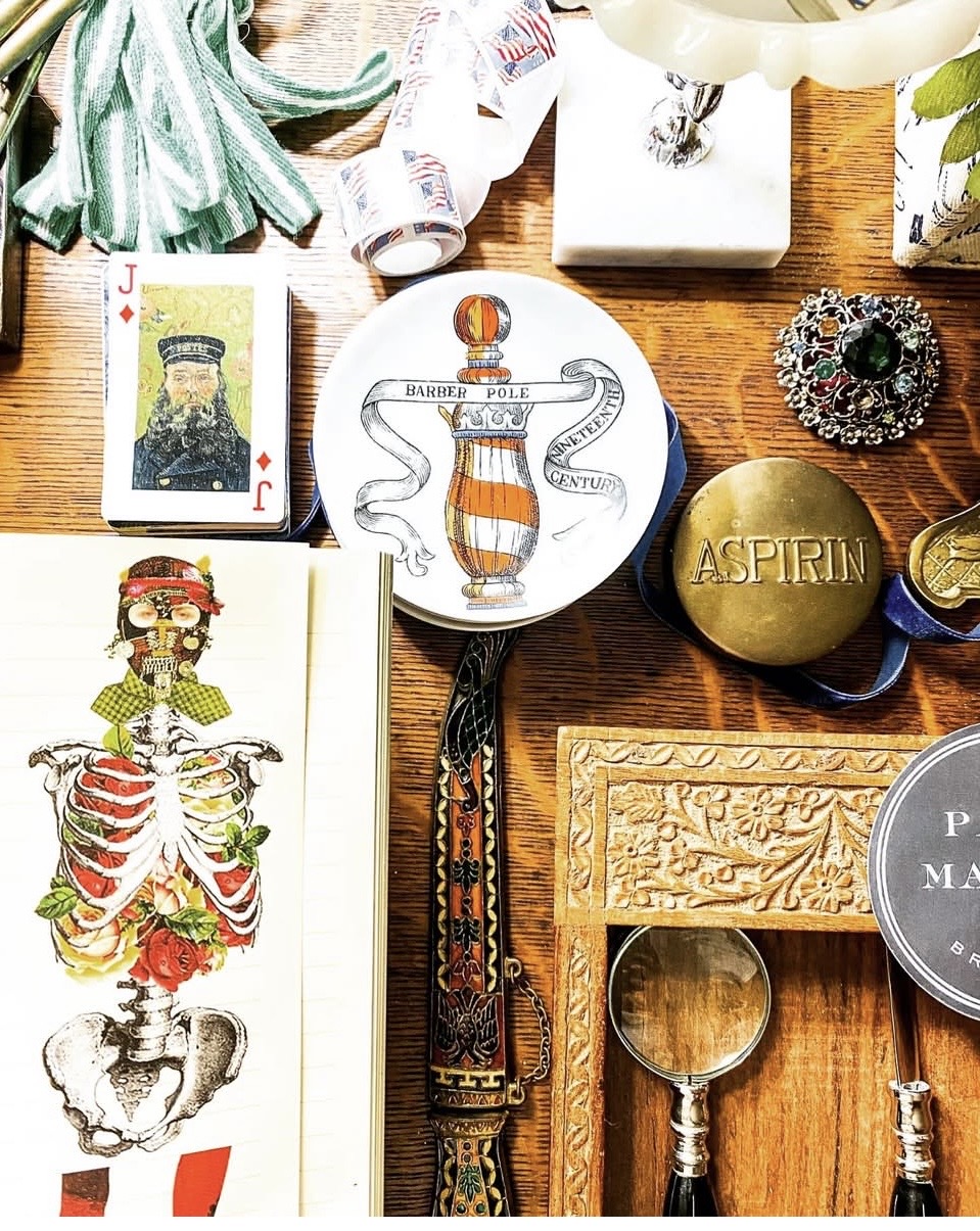 Flat lay of vintage items including a skeleton illustration, a snake and skull plate, aspirin, a magnifying glass, and decorative objects.