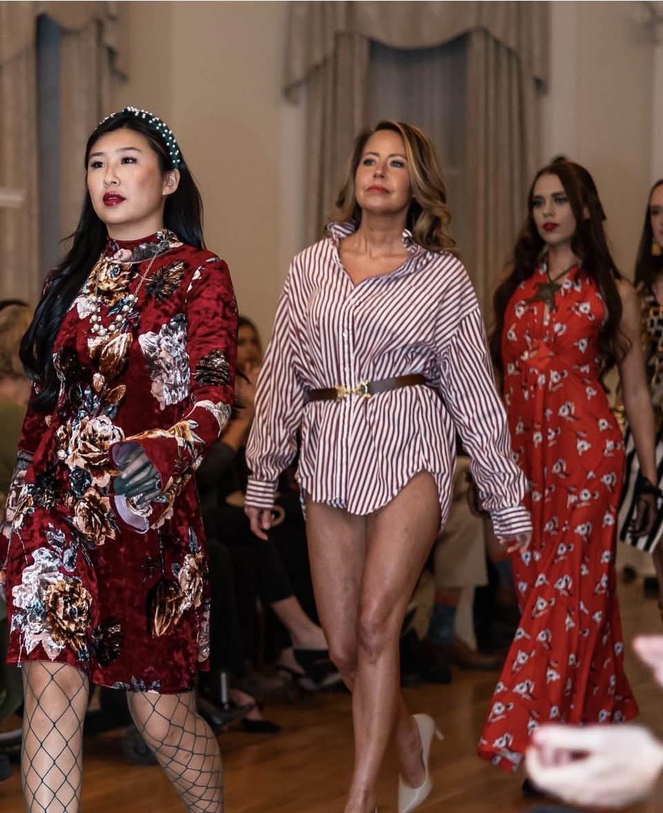 Three women in fashionable outfits walking indoors, with curtains and a wooden floor in the background.