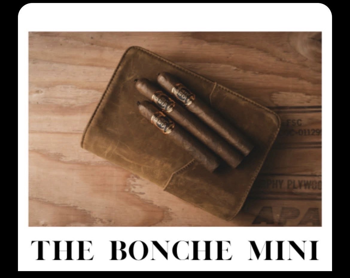 A brown leather wallet with three cigars on top, placed on a wooden surface, with text below reading 'THE BONCHE MINI'.