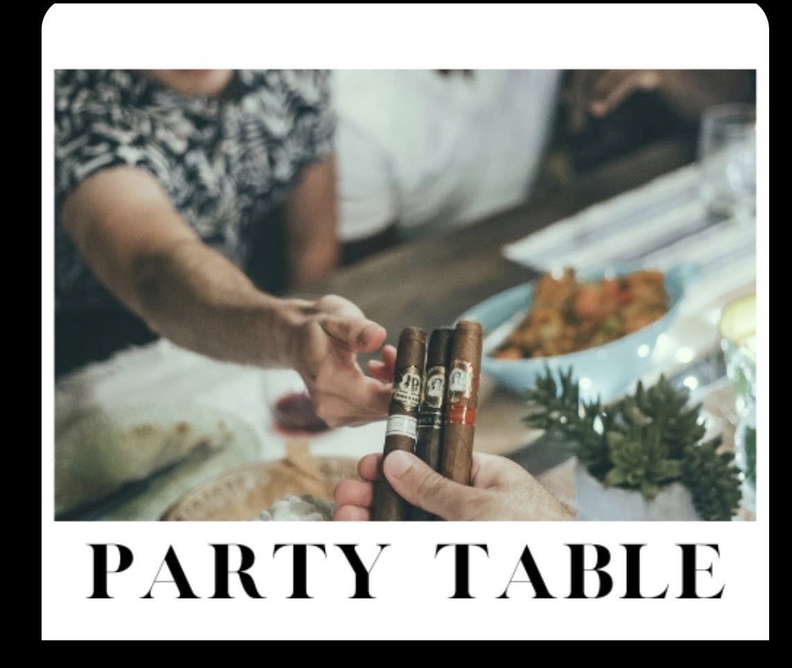 People exchanging cigars at a party table with food and decorations, celebrating together.